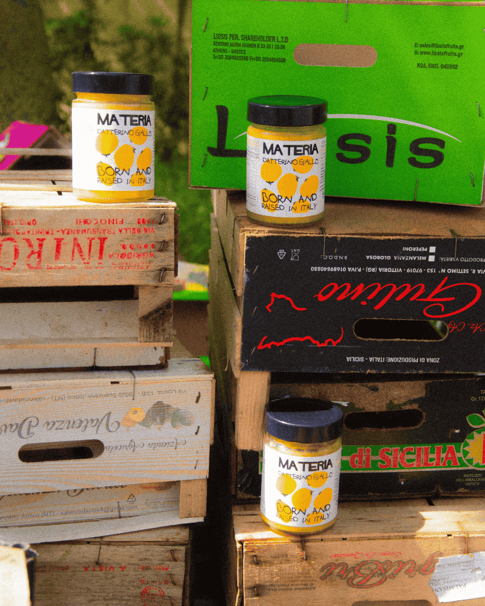 Gläser mit gelber Tomatensoße Datterino Giallo von Materia stehen auf hölzernen Obst- und Gemüsekisten.