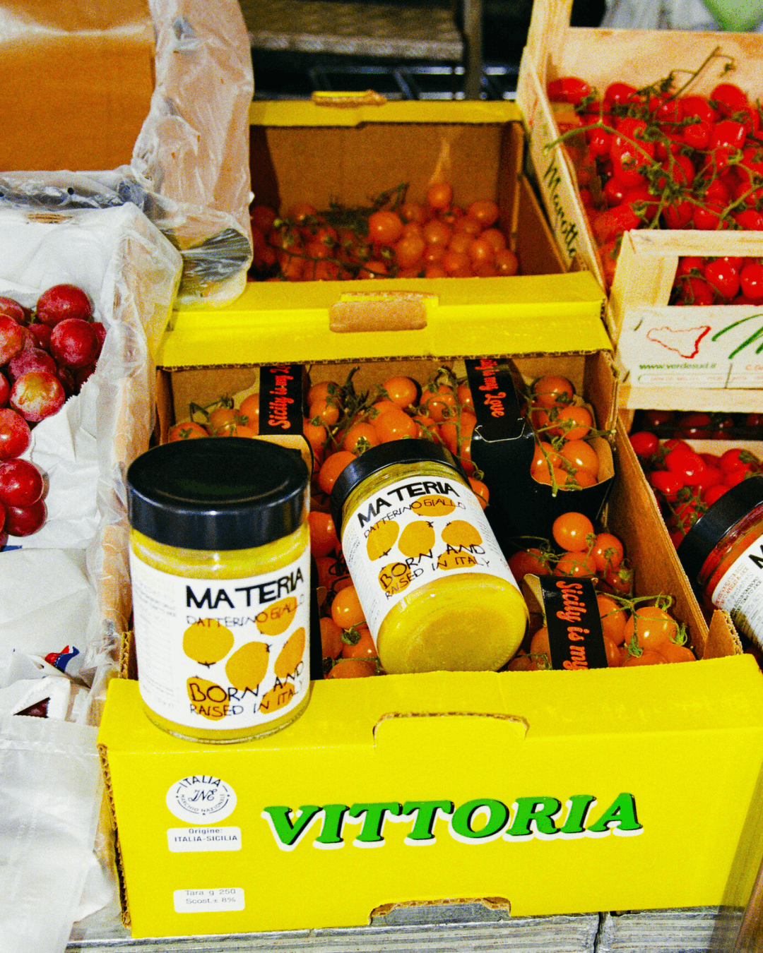 Gläser mit gelber Tomatensoße Datterino Giallo von Materia auf einem Markt auf einer Kiste mit Tomaten.