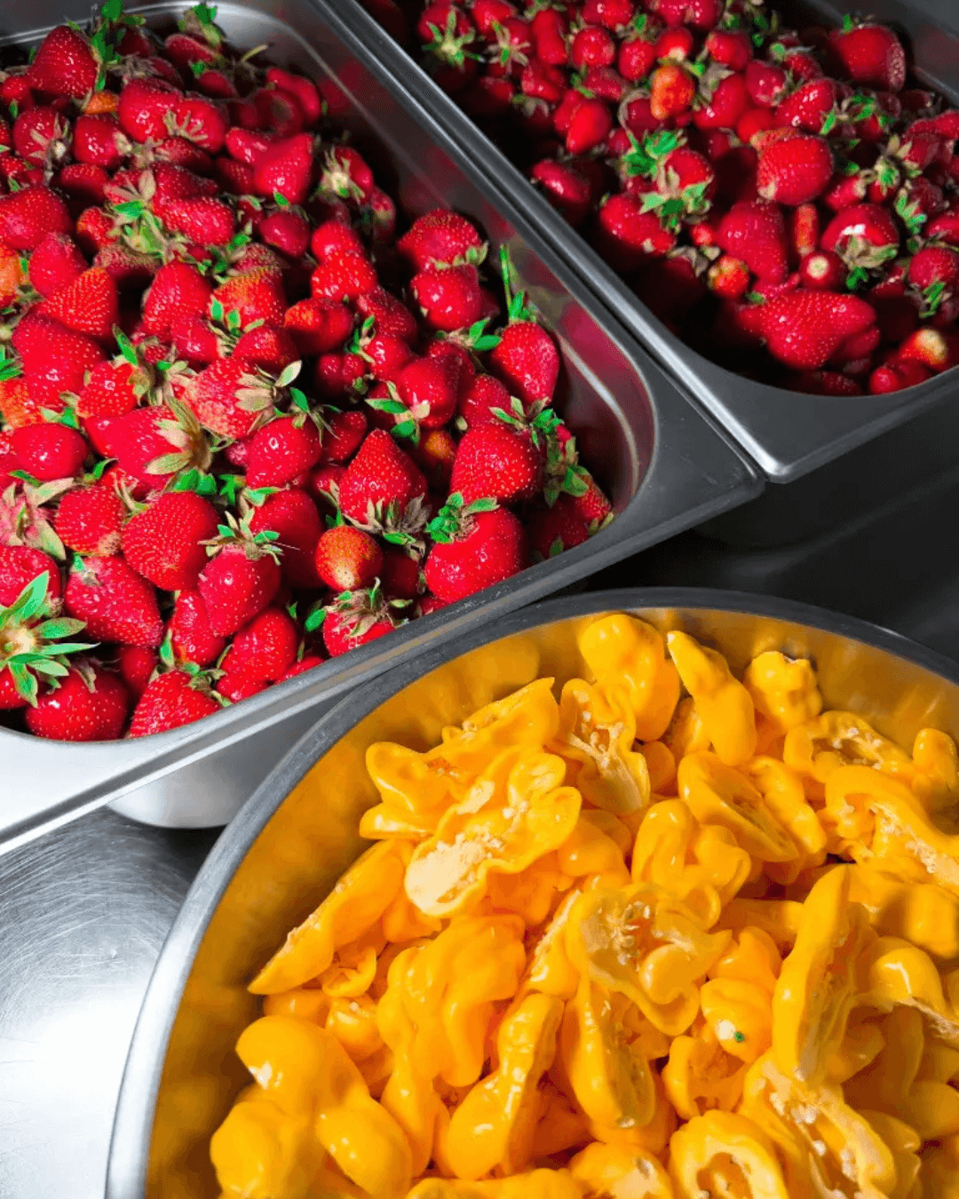 Frische Erdbeeren und gelbe Chilis in Edelstahlbehältern zur Herstellung von Hot Sauce.
